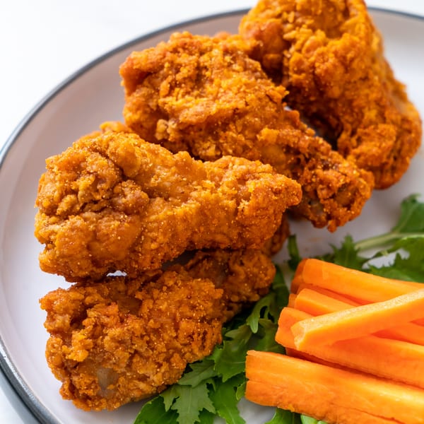 Crispy fried chicken pieces with fresh green lettuce and carrot sticks on a white plate.