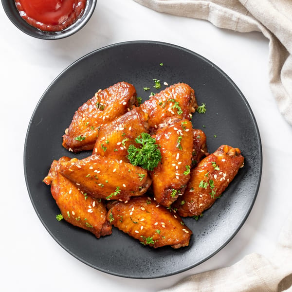 Fried CTs' glazed fried chicken wings with sesame seeds and parsley on a black plate.