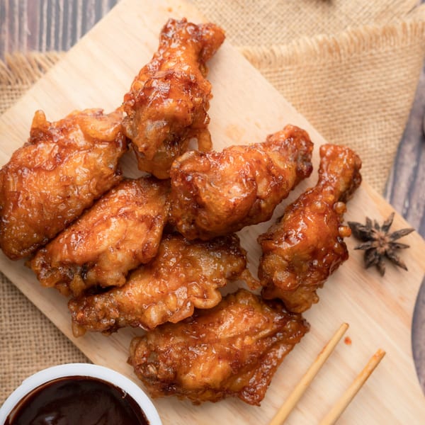 Fried CTs' glazed fried chicken wings on a wooden board with sauce and chopsticks.