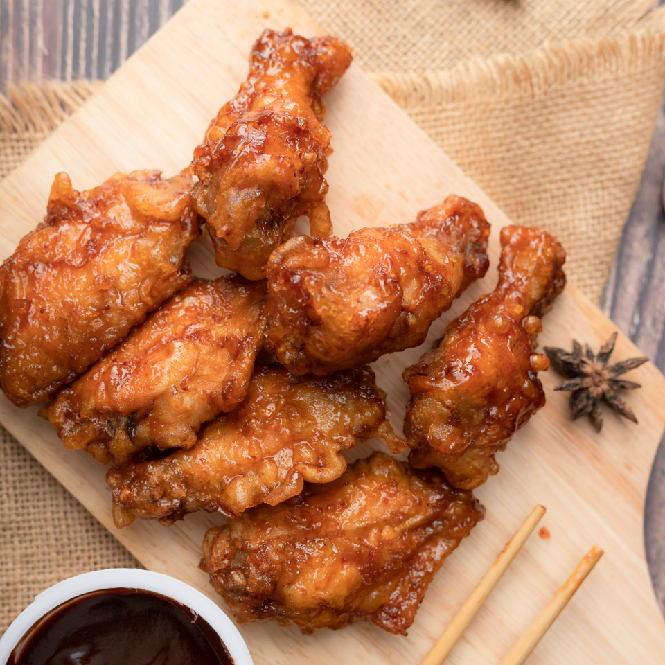 Fried CTs' glazed fried chicken wings on a wooden board with sauce and chopsticks.