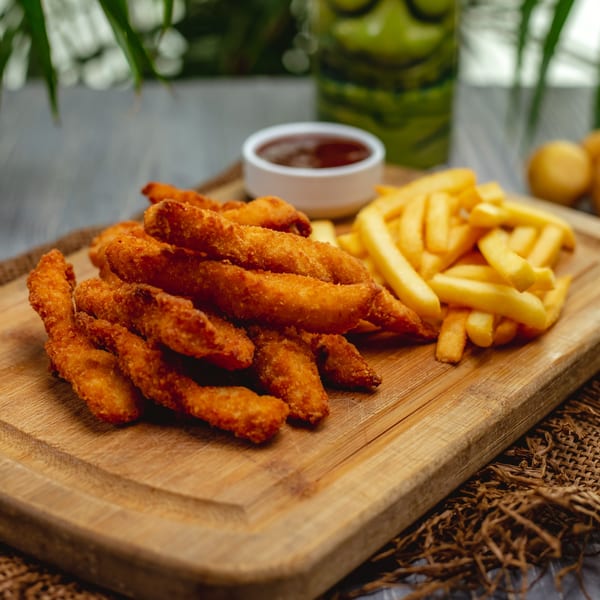 Fried chicken tenders, french fries, and dipping sauce on a wooden board.